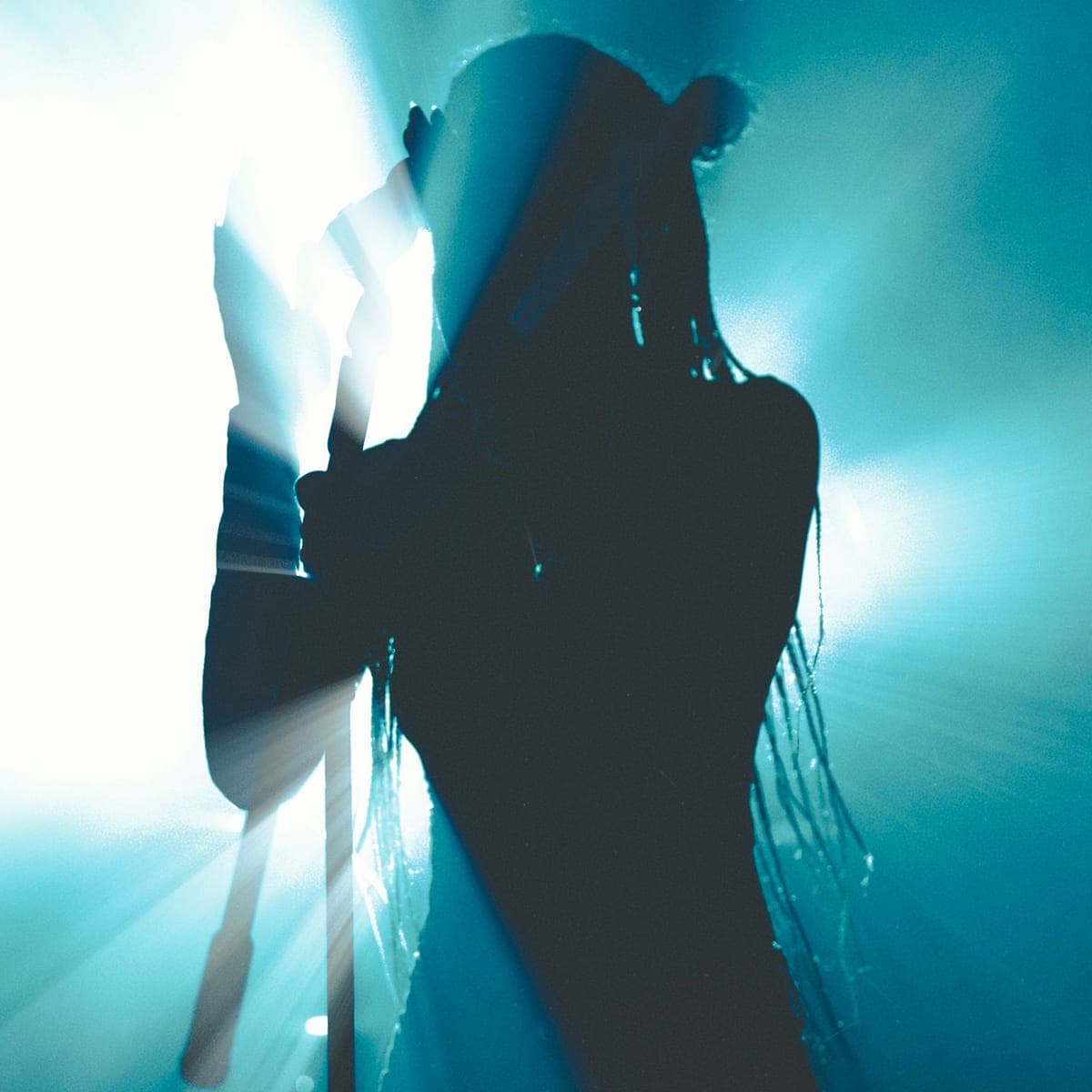 A performer silhouetted against a teal backlight on stage.