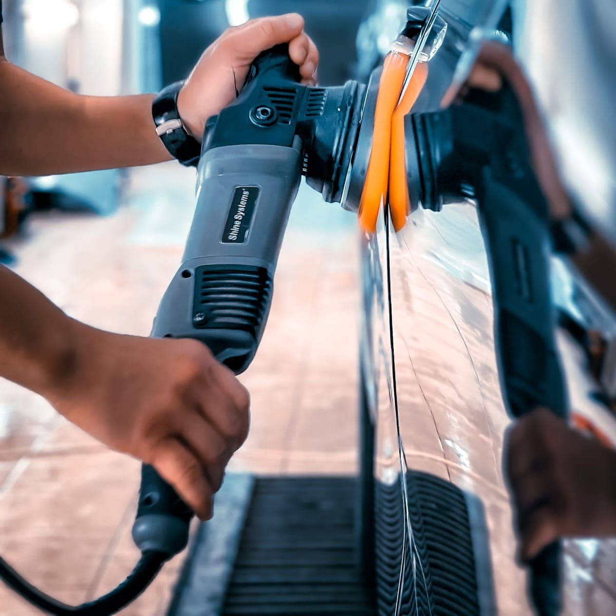 A detailer running a dual-action polisher across a glossy panel.