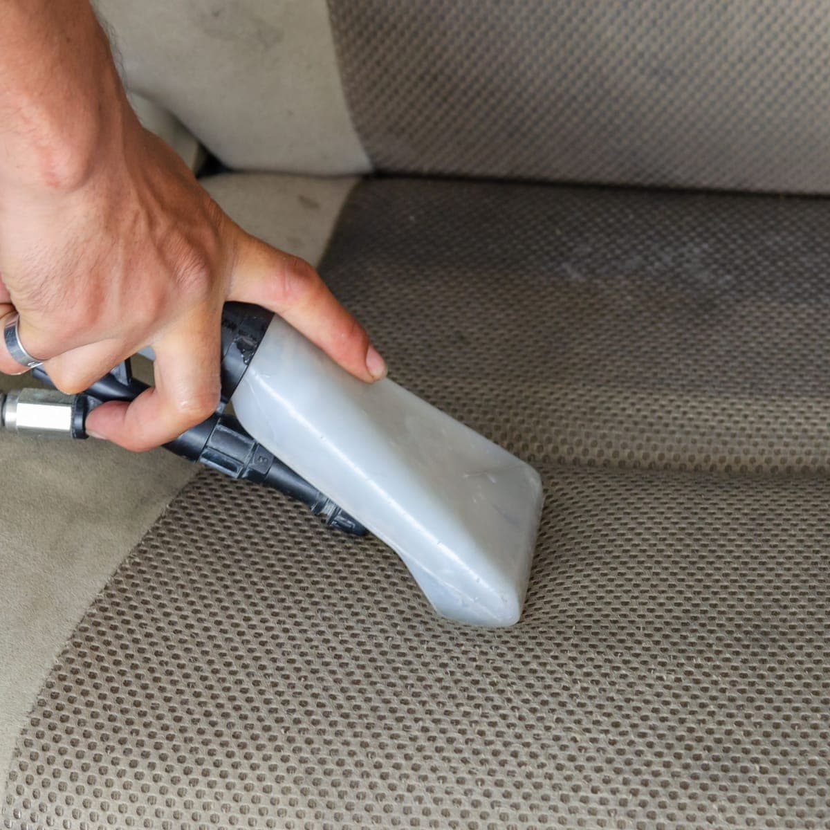 An extractor nozzle lifting dirt out of a fabric seat.