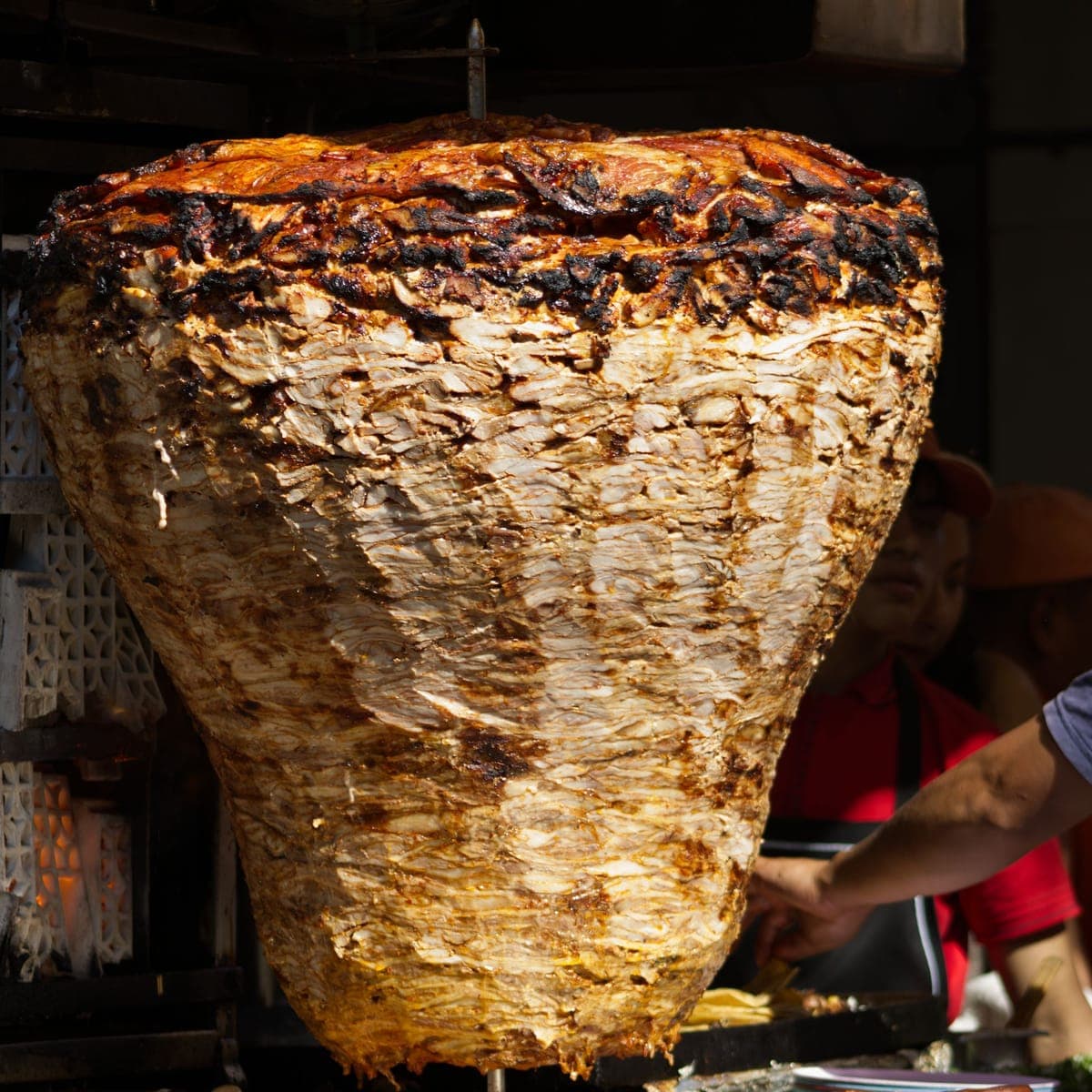 A trompo of al pastor turning beside the griddle.